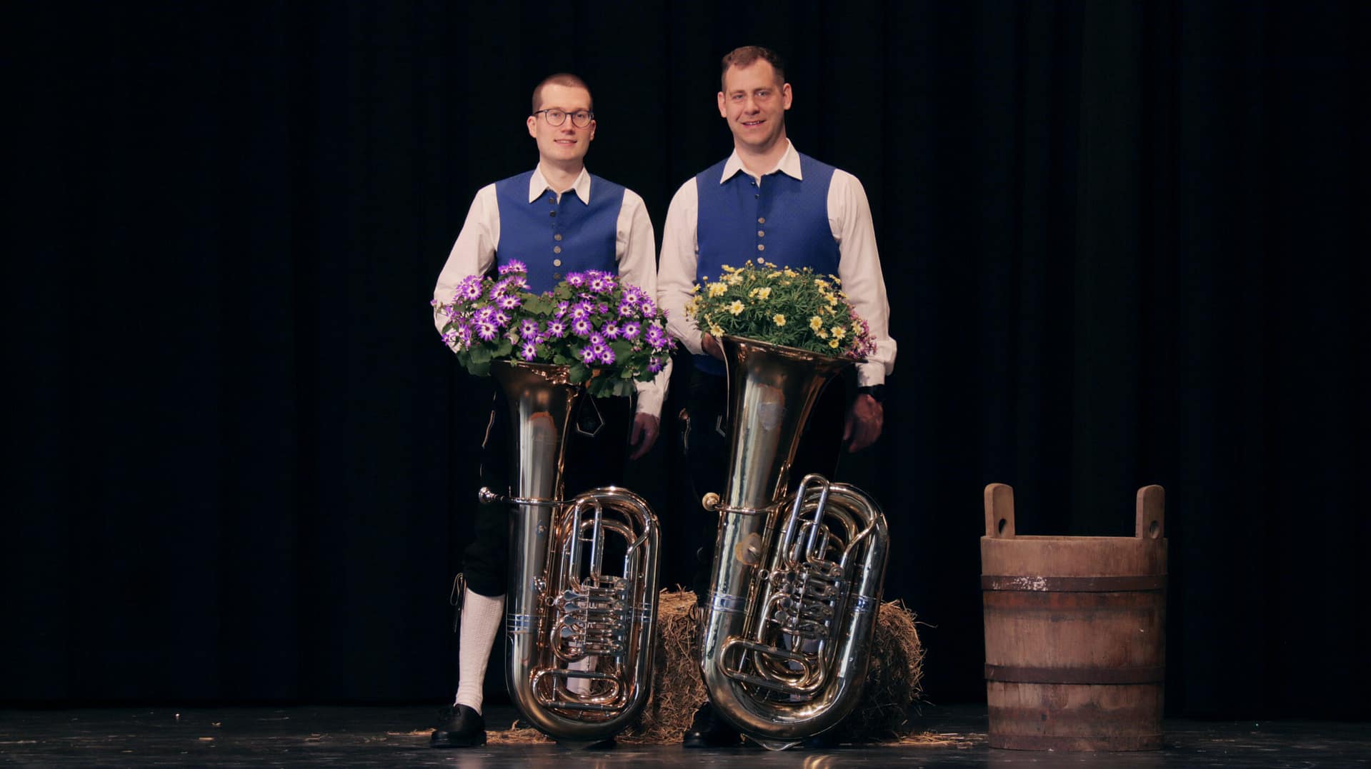 Zwei Männder mit jeweils einer Tuba. Gekleidet in der Tracht des Musikverein Burlafingen. In den Tuben sind Blumen.